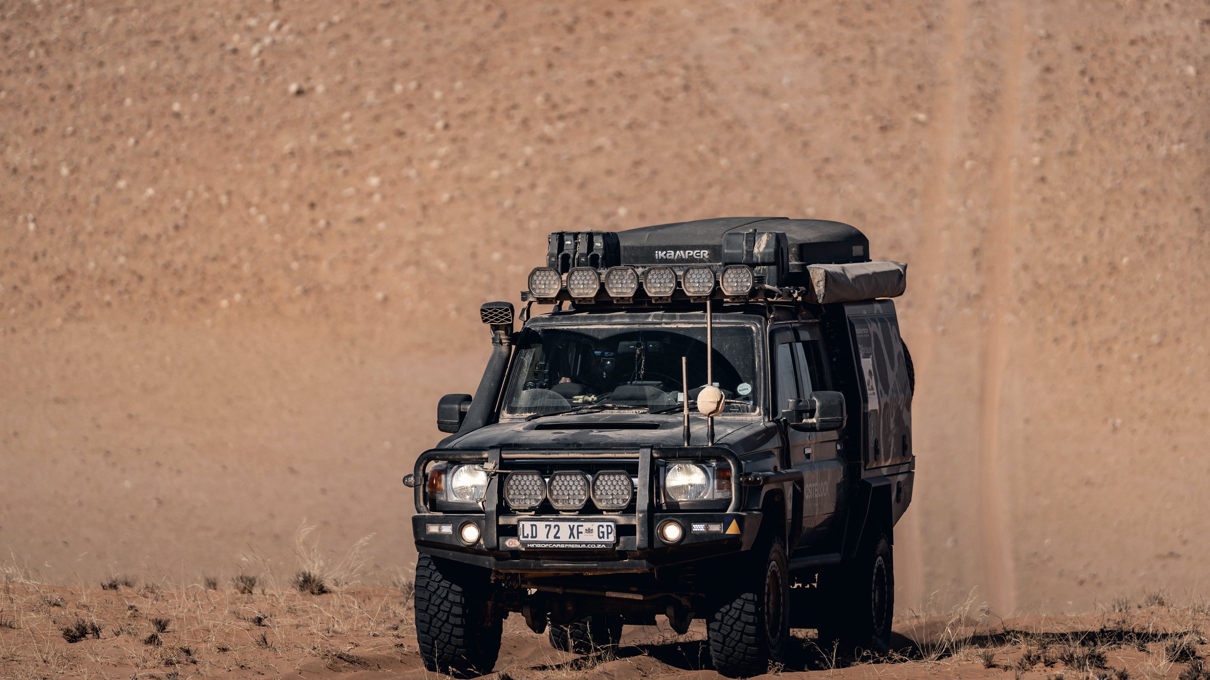 A Land Cruiser with a snorkel driving on a dusty sand track.