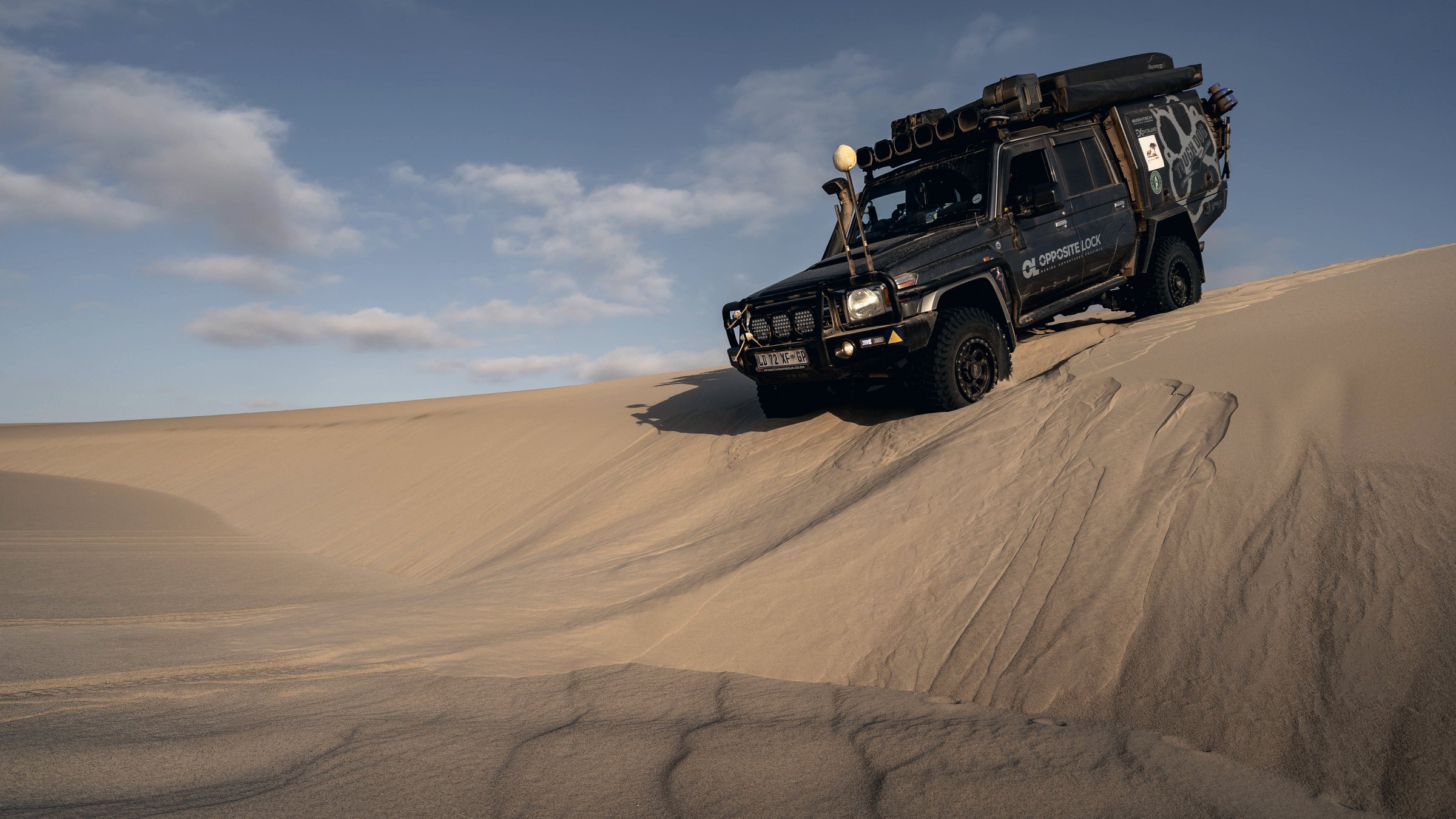 An Opposite Lock Land Cruiser 79 descending a steep dune face, with the snorkel visible running up the passenger-side windscreen pillar.