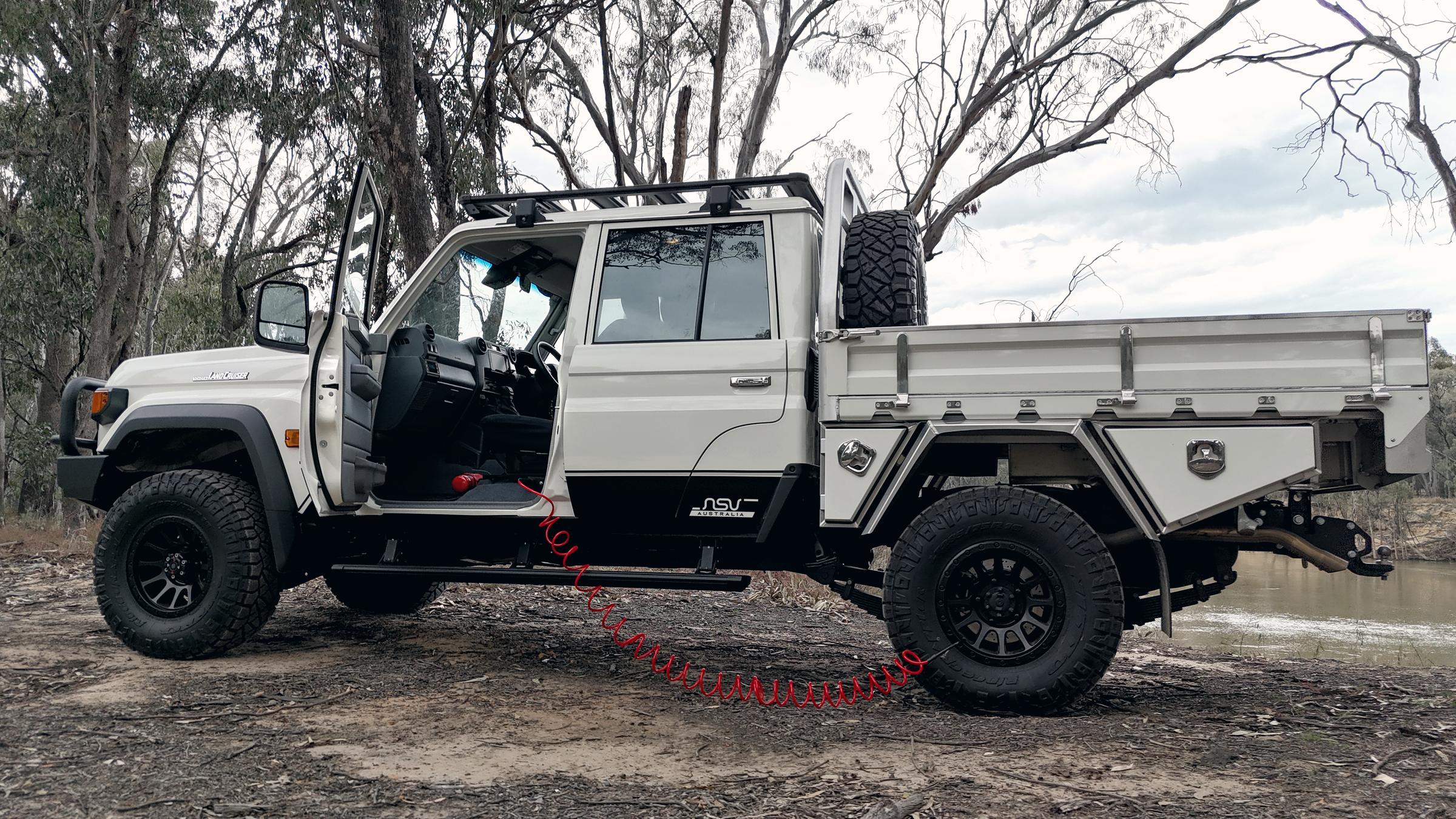 A Land Cruiser ute parked on gravel with a coiled air hose running from the vehicle to a tyre.