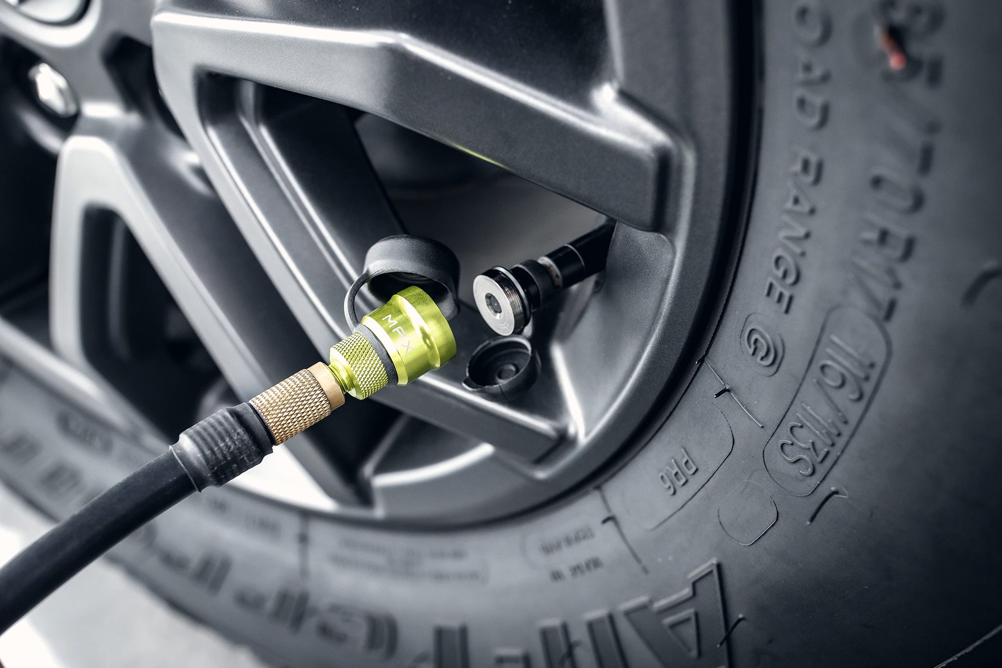 A close-up of a tyre deflator attached to the valve of an all-terrain tyre, with the load rating markings visible on the sidewall.