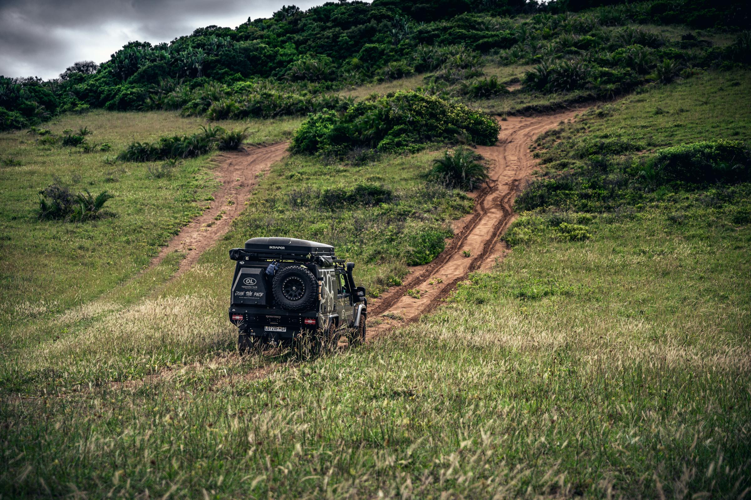 A kitted 4x4 with a rooftop tent on a two-track route through coastal grassland.